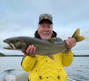 A man in a yellow jacket holds up a Lake Trout after catching it at Anderson's Lodge