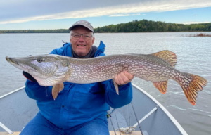 A male Anderson's Lodge guest holds up a large Northern Pike he caught while visiting in 2021